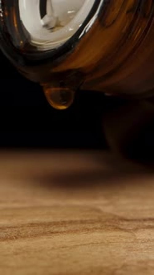 Vertical video. An empty black alcohol bottle with a white pourer in the neck and a drop of whiskey
