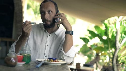 Young man chatting on cellphone enjoying a tasty lunch meal in a cafe