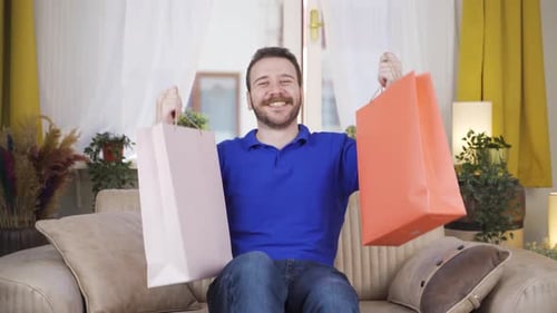 Cheerful Man Displaying Shopping Bags on Sofa