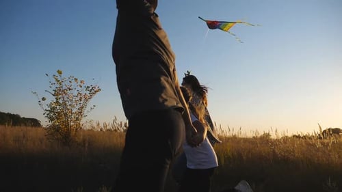 Mom and Dad with Little Daughter Jogging with Rainbow Kites on Rural Trail at Sunset
