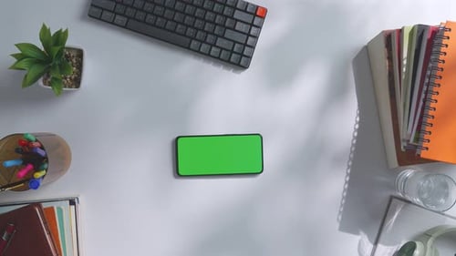 Top down view of a mock up green screen smartphone on a white office desk