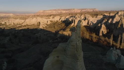 Vol de drone entre des formations rocheuses inhabituelles allongées ressemblant à des cheminées ou à des phallus, illuminées