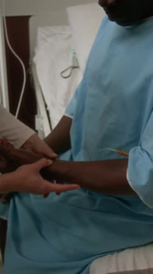 Nurse Checking IV Line of her Patient, Man in Gown Sitting on Bed in Hospital