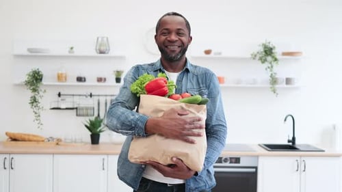Smiling Man Holding Bag of Groceries in Kitchen