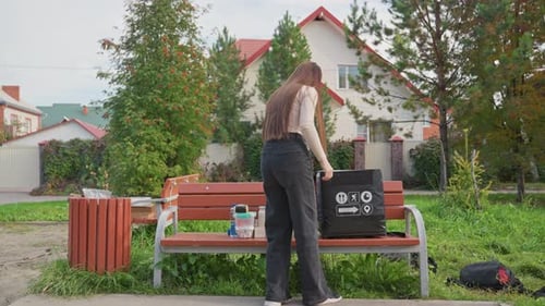 Una mensajera inspecciona su pedido de comida en medio del entorno de un parque suburbano, una joven que entrega a domicilio