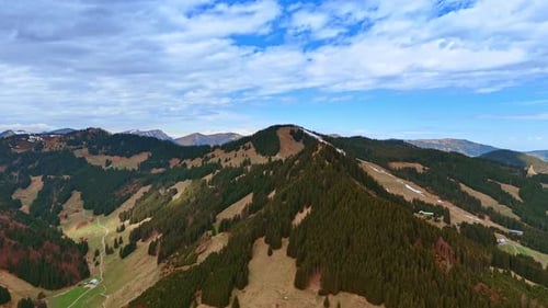 Mountains with wooded areas and bare grassy ones. Rocky background under the cloudy sky.