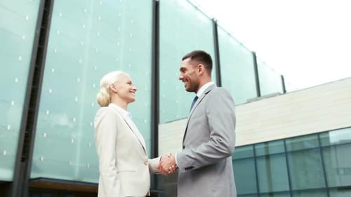 Smiling businessman and businesswoman shake hands on a sunny city street for success