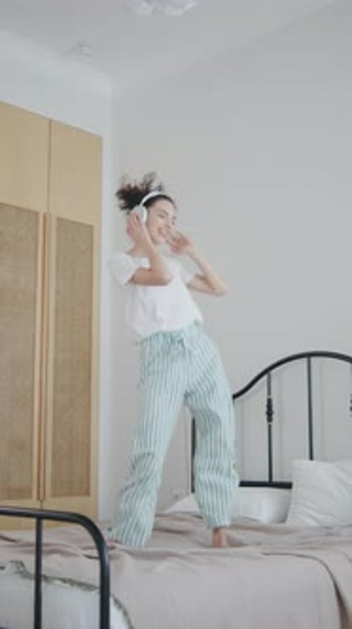 Young Woman Enjoying Music While Dancing on Her Bed in a Bright Bedroom During the Daytime
