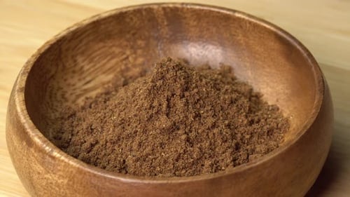 Dried nutmeg spice lies in wooden bowl and rotating on wooden board. Dry seasoning in spoon. Spice