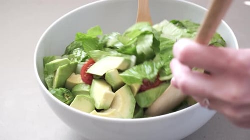 Cooking green salad with avocado and cherry tomatoes in white bowl.