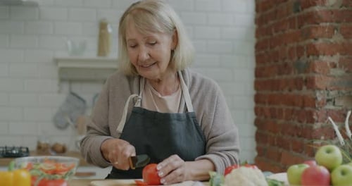 Woman Smiles as She Cuts a Tomato in Kitchen