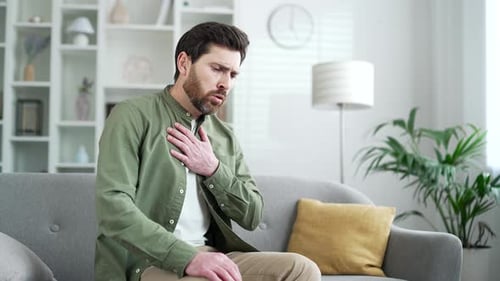 Kranker Mann mit Brustverspannungen und Herzinfarkt, der zu Hause auf dem Sofa im Wohnzimmer sitzt. Reif