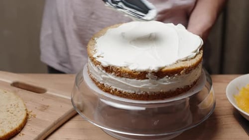 A woman in a slow-motion shot spreads cream over a sponge cake.