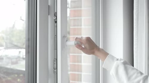 A woman's hand turns the handle of the window frame and opens the plastic window