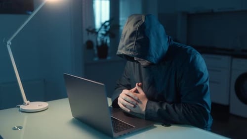Anonymous Hacker Working on His Laptop in a Mysterious and Dark Setting