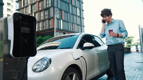 Suitclad Geschäftsmann mit fortschrittlichem Ehrgeiz stützt sich auf sein Elektrofahrzeug