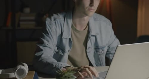 Young Man Working on Laptop in Dimly Lit Room