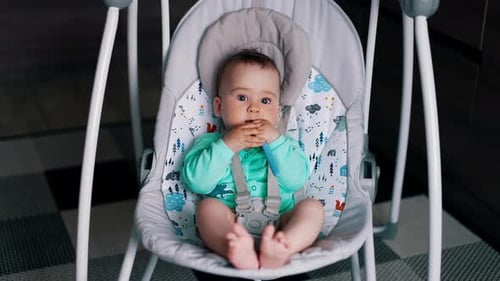 Baby Sits in Bouncer Swing Holding a Toy