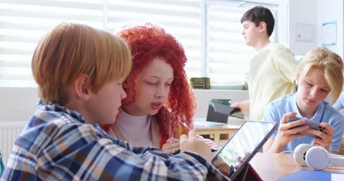 Elementary School Girl Explaining Task to Male Classmate on Digital Tablet While Sitting at Desk