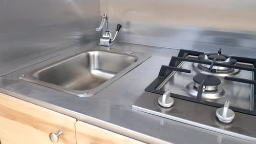 Kitchen and stove area of new deluxe metal teardrop travel trailer on a camping trip.