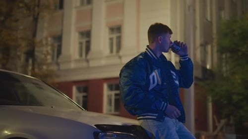 Man Leans On Car Drinking At Night In City