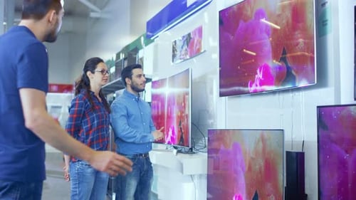 In the Electronics Store Professional Consultant Approaches Young Couple with His Expert Advice on