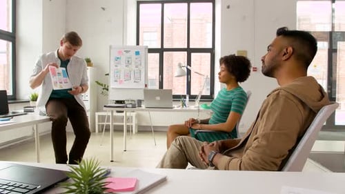 Man presenting user interface mockup to creative team at modern office