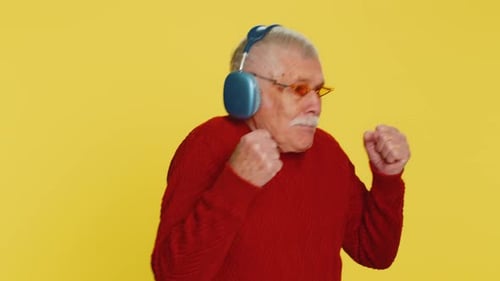 Joyful Senior Man Dancing with Headphones on Yellow