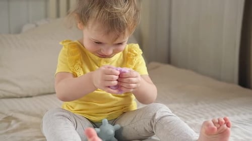 Blonde Child Plays with Textured Ball on Bed