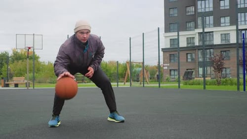 Player Practices Shooting Near Fenced Court Autumn Day with Man Practicing Basketball Skills Outside