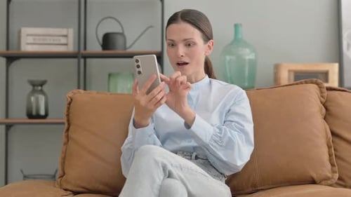 Woman Using Smartphone Celebrates Success on Sofa