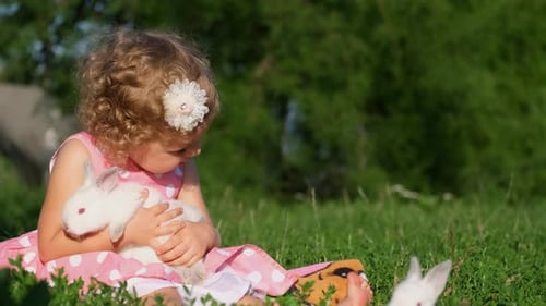 A Beautiful Curly Little Girl is Playing with a White Hare in the Garden