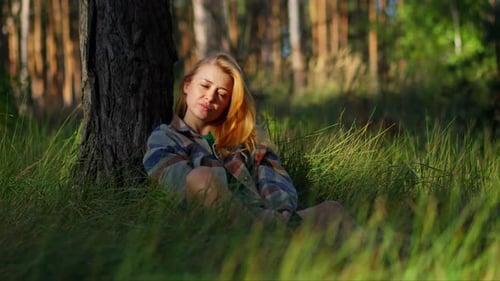 Peaceful girl sits resting and relaxing sitting on the grass in a park, concept of relaxation