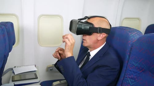 Using a VR virtual reality headset on a plane. A mature business man is using VR whist sitting in th