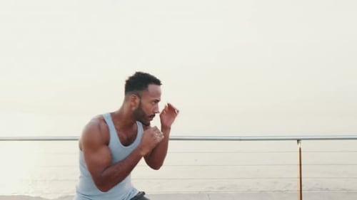 Young fit athlete boxer practicing punching technique while standing on the embankment