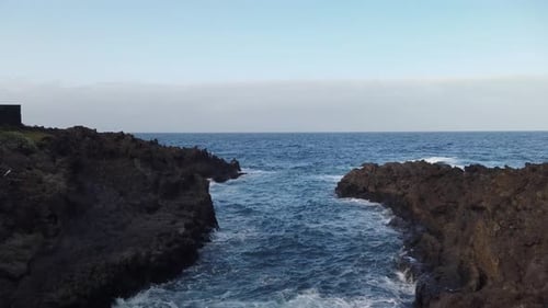 A static shot of an inlet from the ocean between black volcanic rocks
