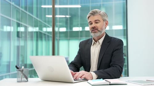Smiling mature businessman working on a laptop sitting at workplace in business office.