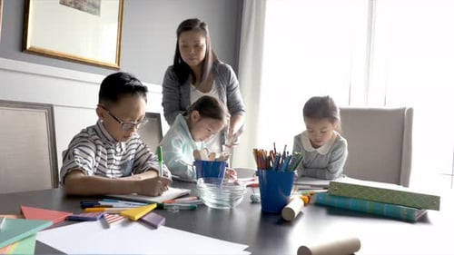 Mother home schooling children at dining table with art and crafts