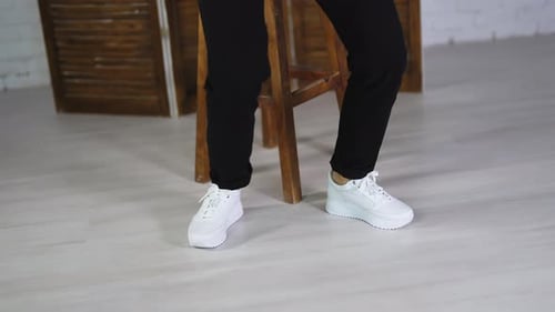 Woman wearing black trousers dances in white sneakers.