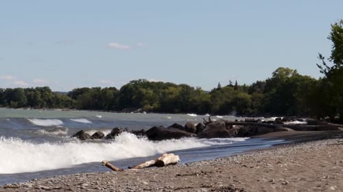 Waves gently crashing along a rocky shoreline, from left to right, with lots of blue sky visible.