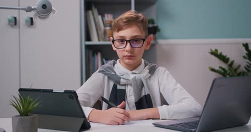Portrait of smart boy doing homework on laptop computer in modern room at home Looking at camera.