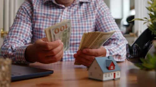 Man Counting Money at Table with Miniature House