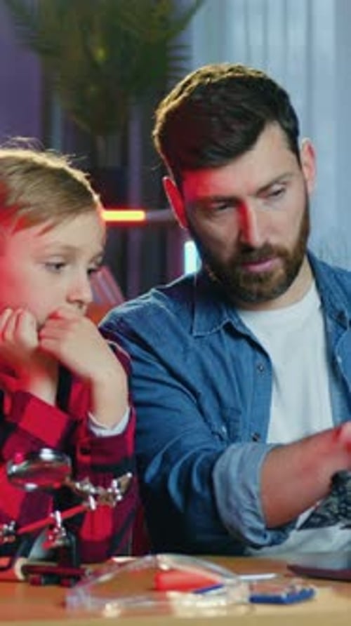 Father and Daughter Examine Circuit Board at Table