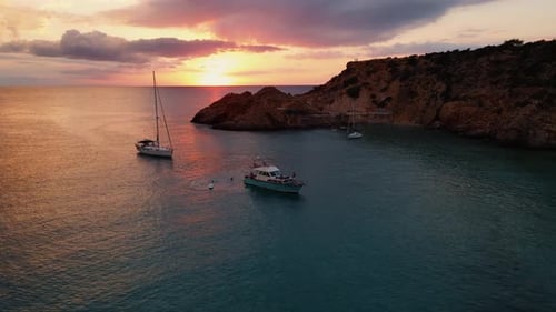 Aerial: sail boats and yacht anchored at the bay of Cala Tarida, Ibiza, Spain during sunset.