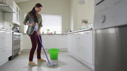 Happy caucasian woman cleaning floor with mop and bucket of water at home