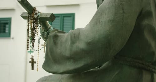 Statue with Arm Extended Holding Cross Covered in Prayer Beads Near Shuttered Windows in Atrani