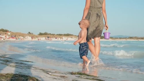 Happy unrecognizable woman and son walking on a beautiful sandy beach at sunset