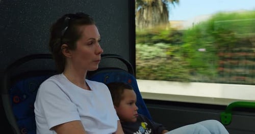 Thoughtful Mother Travels By Bus with Cheerful Son Admiring View From Window