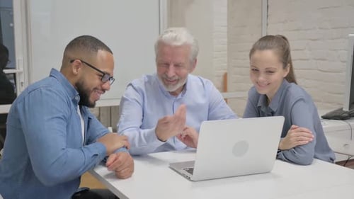 Colleagues laugh and share a laptop at work