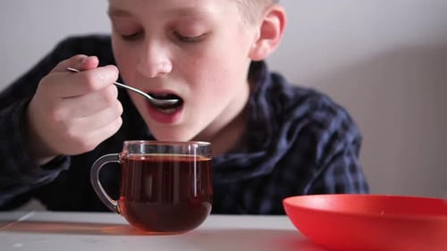 Boy Drinking Tea with a Spoon at Table